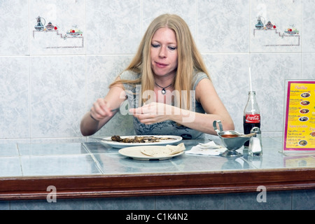 Piuttosto giovane donna messicana con lunghi capelli biondi si siede a mattonella pulita contro di mangiare il pranzo in Benito Juarez di mercato Messico Oaxaca Foto Stock