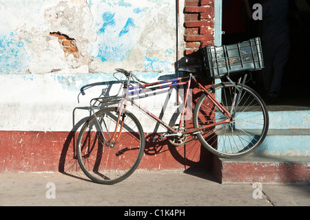 Vecchia bicicletta appoggiata contro indossato incrinato delicatamente colorato intonaco esterno muro con porta aperta e passaggi in Oaxaca Messico Foto Stock