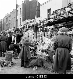 1950s, una fotografia di J Allan Cash di un commerciante presso la sua bancarella di frutta e verdura al mercato all'aperto di Camden Town, Londra. Foto Stock