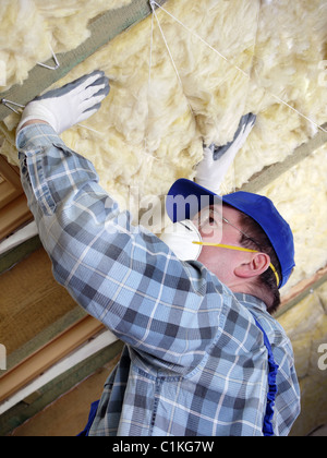 Lavoratore isolante termicamente una soffitta della casa utilizzando la lana minerale Foto Stock