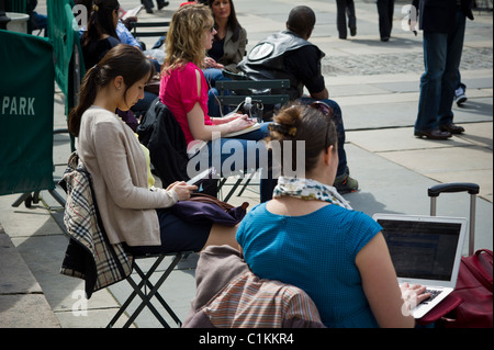 Un lettore utilizza il suo Amazon Kindle libro elettronico mentre altri utilizzano un laptop e lettori musicali in Bryant Park di New York Foto Stock