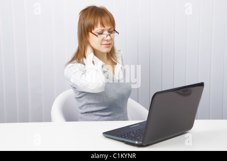 Stanco lavoratore in ufficio. Disheveled Ragazza con notebook. dolore al collo Foto Stock