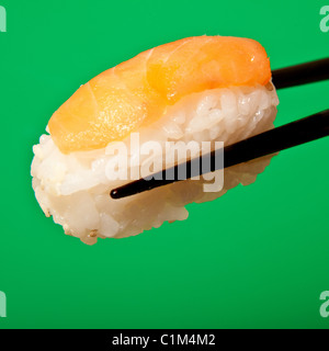 Il nigiri sushi con salmone essendo trattenuto in un paio di bacchette. Foto Stock