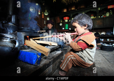 Little Boy accendere un fuoco in una casa tradizionale nelle colline nepalesi Nepal Himalaya Foto Stock