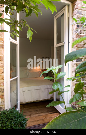 Vista dal giardino attraverso aprire finestre francesi nella camera da letto con pavimento in legno Foto Stock