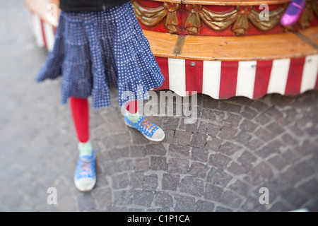 10 anno vecchia ragazza in rosso collant e sneakers sorge accanto ad una giostra mentre la sorella ottiene una corsa. Foto Stock