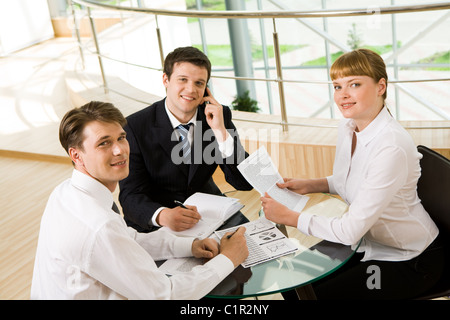 Foto di successo della co-lavoratori riuniti intorno al tavolo e guardando la telecamera durante la riunione Foto Stock