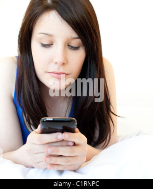 Concentrato di giovane donna texting mentre giaceva su un letto Foto Stock