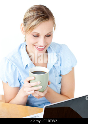 Sorridente imprenditrice di bere il caffè usando il suo computer portatile al tavolo della colazione Foto Stock