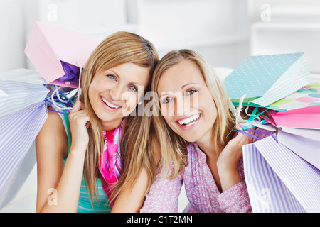 Incandescente due donne azienda shopping bags sorridente verso la telecamera Foto Stock