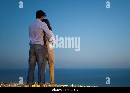 Matura in piedi sul bordo della piscina a sfioro di crepuscolo, guardando il mare Foto Stock