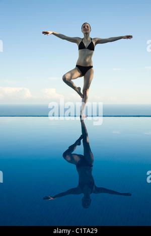 Donna in piedi in posa ad albero sul bordo della piscina a sfioro Foto Stock