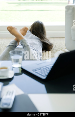 Giovane donna sdraiata su stomaco sul pavimento, a guardare fuori dalla finestra Foto Stock