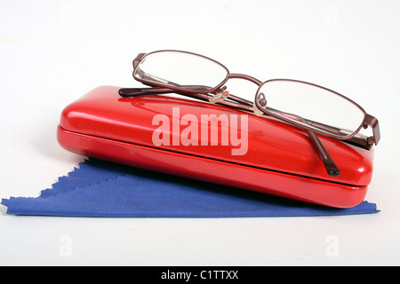 Una coppia di borgogna gli occhiali da lettura su un bianco di fondo tagliato con un rosso custodia per occhiali e panno blu per pulizia. Foto Stock