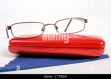 Una coppia di borgogna gli occhiali da lettura su un bianco di fondo tagliato con un rosso custodia per occhiali e panno blu per pulizia. Foto Stock