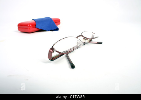 Una coppia di borgogna gli occhiali da lettura su un bianco di fondo tagliato con un rosso custodia per occhiali e panno blu per pulizia. Foto Stock
