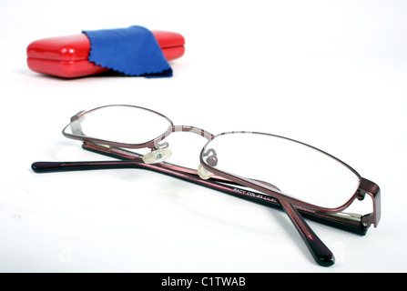 Una coppia di borgogna gli occhiali da lettura su un bianco di fondo tagliato con un rosso custodia per occhiali e panno blu per pulizia. Foto Stock