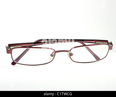 Una coppia di borgogna gli occhiali da lettura su un bianco di fondo tagliato con un rosso custodia per occhiali e panno blu per pulizia. Foto Stock