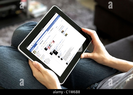 Vista ravvicinata di una donna tenere per mano le persone un ipad lettura suoi newsfeed Facebook in un salotto Foto Stock