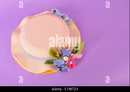 Cibo per Pasqua - Torta di Pasqua conformata come un cofano di Pasqua Hat con fondente glassa e pasta di zucchero fiori isolati su viola Foto Stock