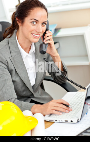 Donna sorridente architetto parlando al telefono e con il suo computer portatile nel suo ufficio Foto Stock