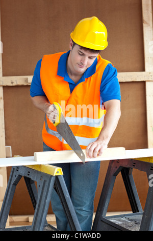 Bello lavoratore di sesso maschile che indossa un casco giallo segagione di un pannello di legno Foto Stock