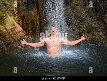 Un uomo che gode di una cascata naturale e piscina. Foto Stock