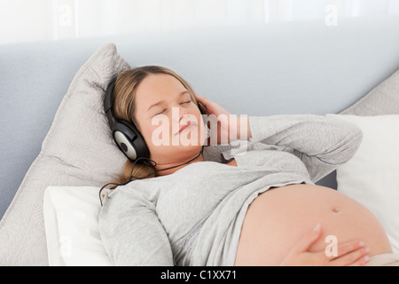 Piuttosto futura mamma ascoltando musica giacente su un letto Foto Stock