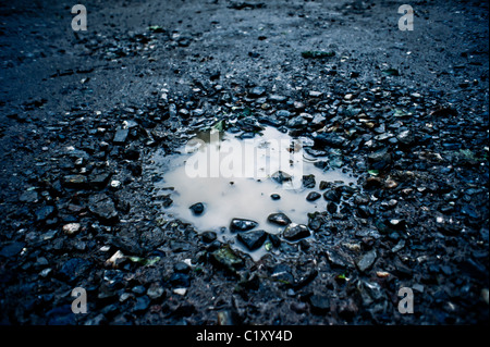 Una buca nella strada piena di acqua di pioggia Foto Stock