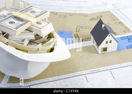 Close-up della casa giocattolo modello su blueprint con casco pieno di dollari nelle vicinanze Foto Stock