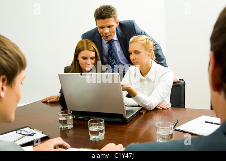Immagine di due dipendenti a discutere di nuova idea mentre l uomo di successo guardando il monitor di un laptop nelle vicinanze Foto Stock