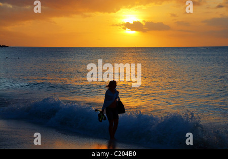 Giovane donna a piedi linea surf Oceano Indiano surf al tramonto, Seicelle Foto Stock