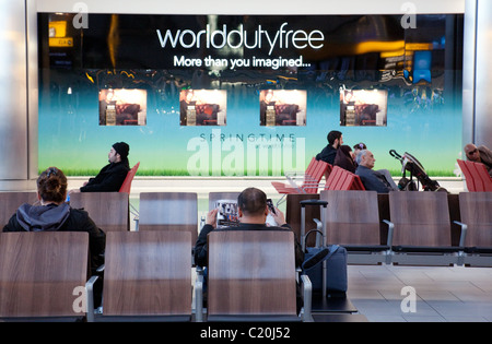 I passeggeri in partenza lounge contro lo sfondo della World Duty Free store, il Terminal 5 di Heathrow, London REGNO UNITO Foto Stock