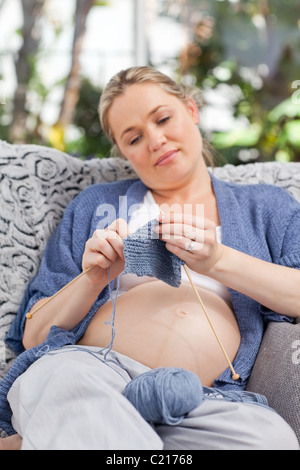 Donna incinta maglia sul suo divano Foto Stock