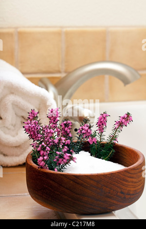 Piuttosto heather fiori in un vaso di sali di Epsom in una vasca da bagno bordo pronto a fare il bagno. I sali di Epsom con viola heather fiori in un vaso di legno vicino a una vasca da bagno Foto Stock