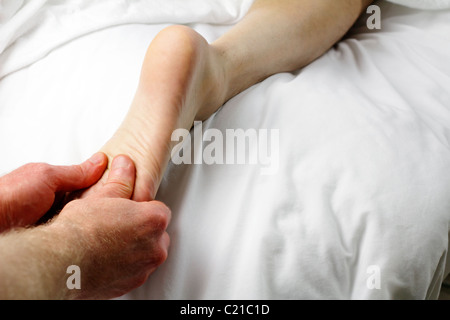 Maschio terapista di massaggio un massaggio dei piedi di un client. Un piede di un uomo che stabilisce con il lato stampato rivolto verso il basso essendo zona riflessologia massaggiato dal terapista di massaggio Foto Stock