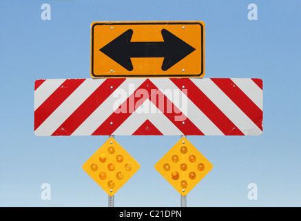 Doppia freccia lato riflettente e cartelli di avviso in corrispondenza di una giunzione a T su una strada Foto Stock