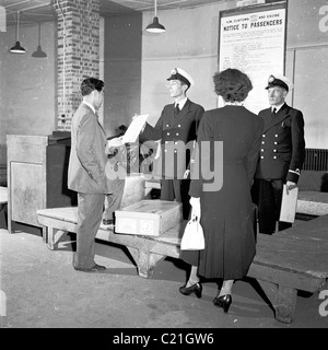 1950, storico, un visitatore d'oltremare appena arrivato in Gran Bretagna che ha mostrato un avviso da parte di ufficiali doganali uniformi ad un controllo del bagaglio, Inghilterra. Foto Stock