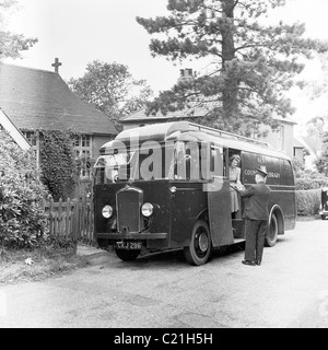 1950s, una biblioteca mobile parcheggiata in una corsia nel Kent, Inghilterra, Regno Unito, con un autista in uniforme con cappello che aiuta una signora con libri sui gradini laterali del veicolo Foto Stock