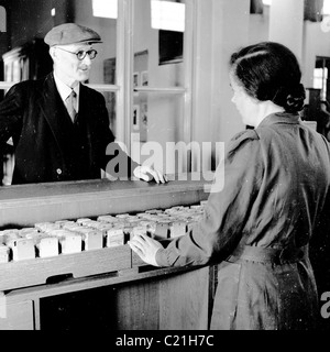 Degli anni Cinquanta, Inghilterra. Elegantemente vestito uomo anziano parla di una femmina in uniforme bibliotecario in questo quadro storico da J Allan contanti. Foto Stock