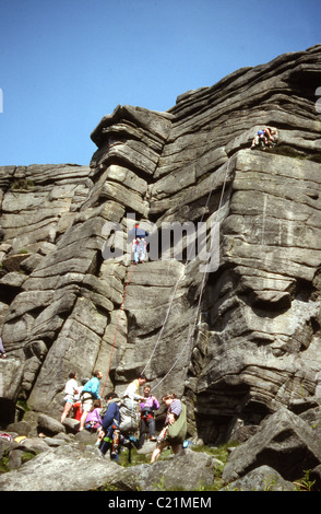 1960s, gruppo di adulti di arrampicata su roccia a Stanage Edge, Derbyshire, Inghilterra, un luogo popolare nel Peak District, famoso per la sua scarpata di pietra arenaria. Foto Stock