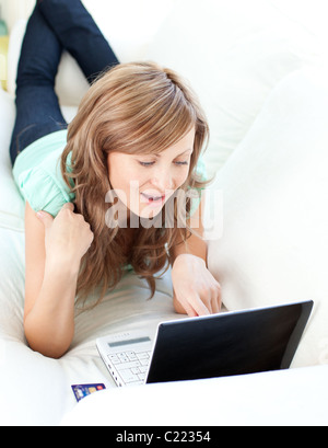 Gioiosa donna bionda guardando il suo computer portatile sul divano Foto Stock