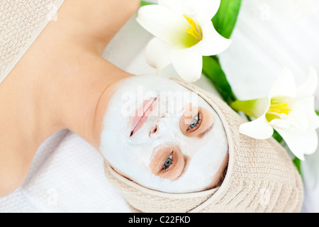 Incandescente donna sdraiata su un lettino da massaggio con crema bianca sul suo viso Foto Stock