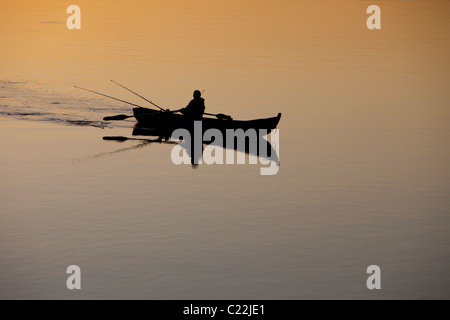 Pescatore che traina da una barca a remi / skiff / dinghy al tramonto sul fiume Oulujoki Finlandia Foto Stock