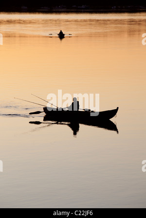 Pescatore che traina da una barca a remi / skiff / dinghy al tramonto sul fiume Oulujoki Finlandia Foto Stock