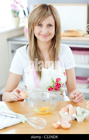 Donna allegra cucina in cucina e rompere le uova Foto Stock