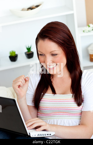 Gioiosa giovane donna con il suo computer portatile seduto su un divano Foto Stock