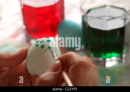 Una giovane donna dipinge con cura macchie su un uovo di Pasqua. Foto Stock