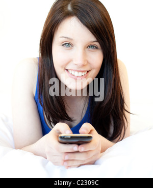 Felice giovane donna texting mentre giaceva su un letto Foto Stock