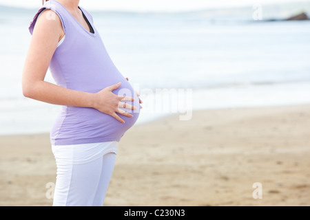 Close-up di una donna incinta in piedi sulla spiaggia Foto Stock